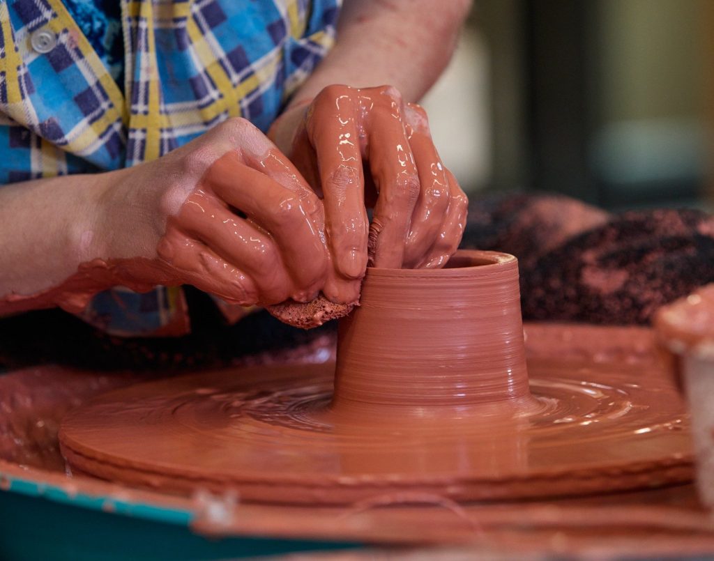 potters hands in red clay at the pottery wheel